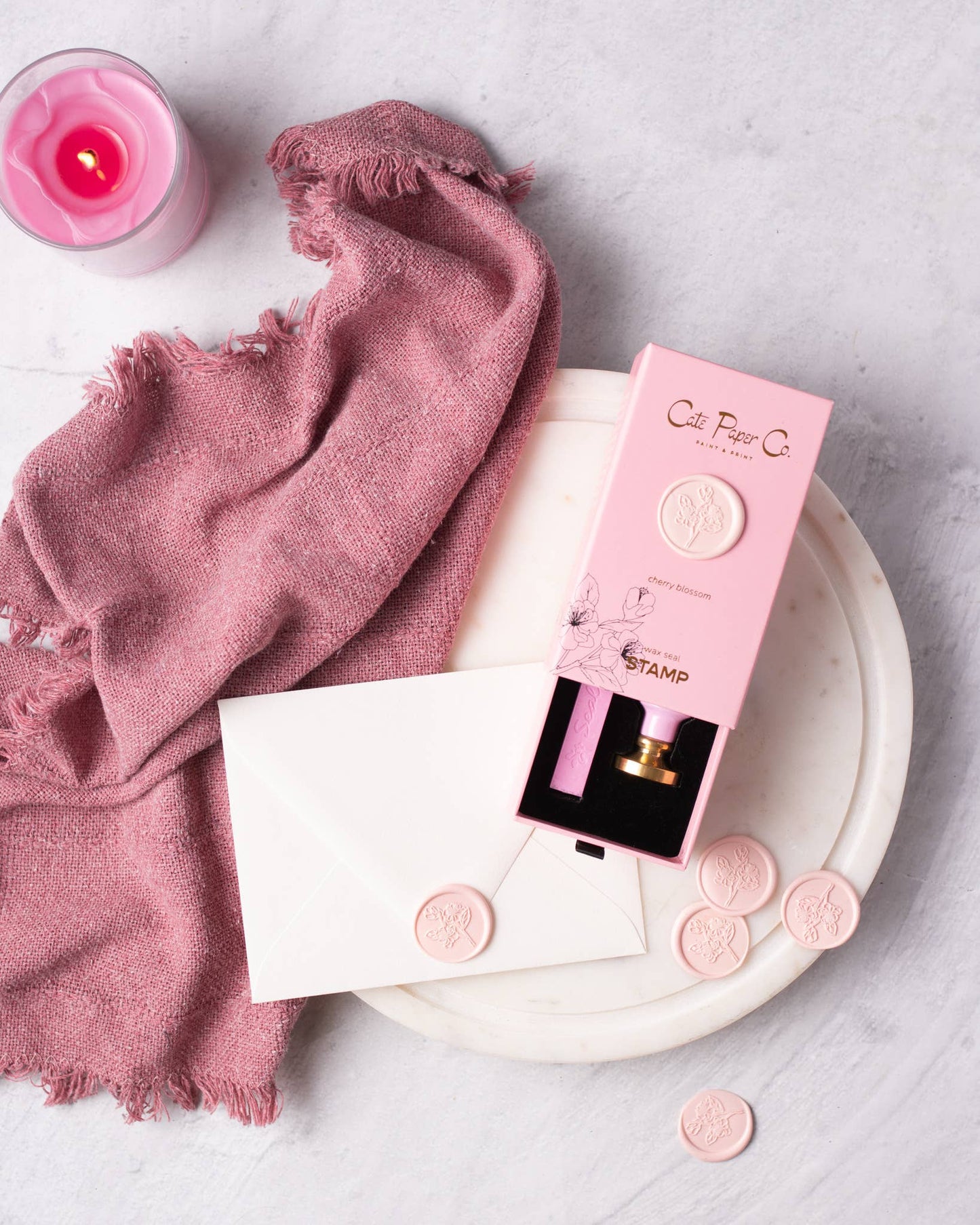 Pink lip balm with packaging on a white plate with a pink cloth and candle in the background