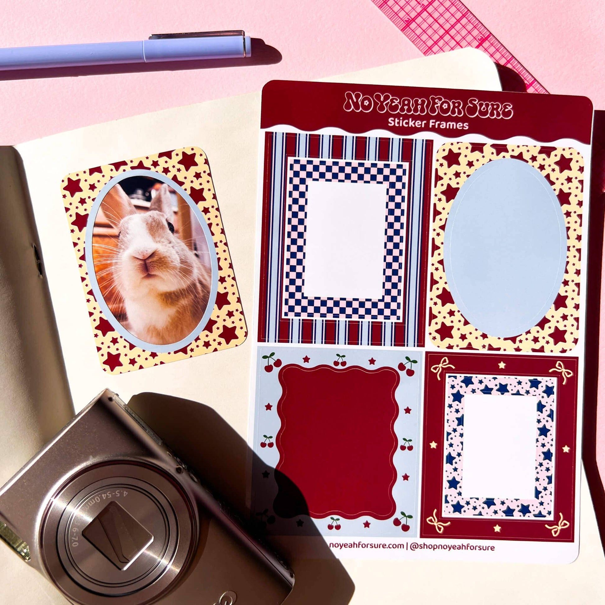 A sheet of decorative sticker frames labeled 'No Year For Sure Sticker Frames' shown on a pink surface with a rabbit photo insert and a camera nearby. The sticker frames include red, navy, white, and gold patterns, and the sheet also shows a sample rabbit photo sticker.
