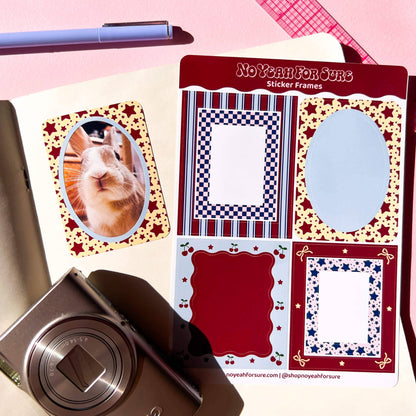 A sheet of decorative sticker frames labeled 'No Year For Sure Sticker Frames' shown on a pink surface with a rabbit photo insert and a camera nearby. The sticker frames include red, navy, white, and gold patterns, and the sheet also shows a sample rabbit photo sticker.