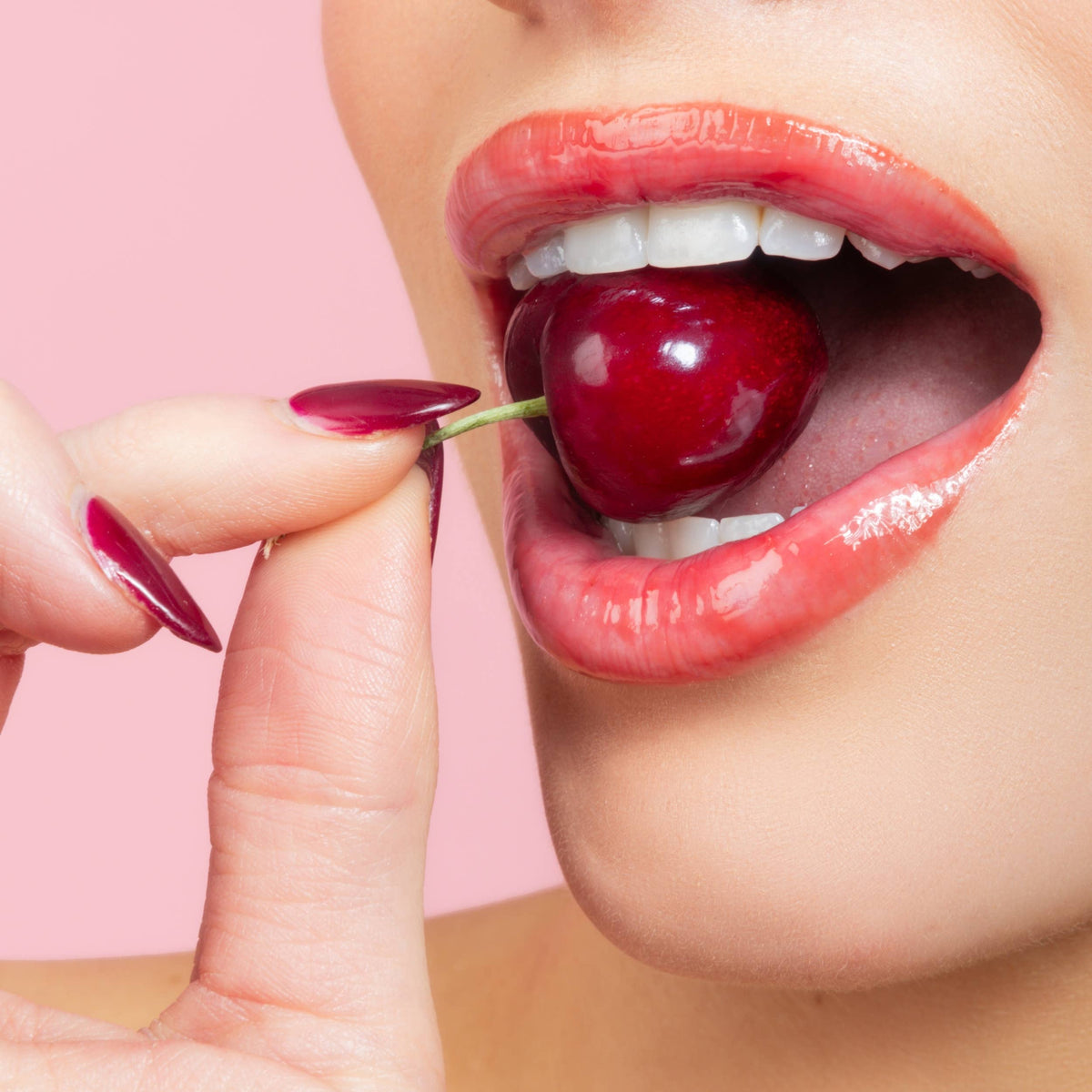 Close-up of a person holding a cherry with a pink background