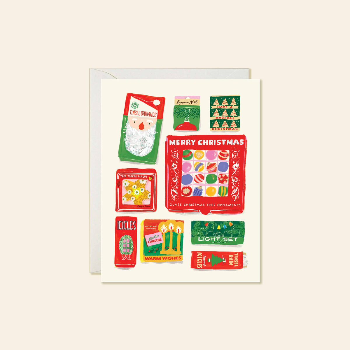 A square Christmas greeting card with a white envelope behind it, featuring a collage of vintage-style holiday illustrations and text including 'MERRY CHRISTMAS' and 'GLASS ORNAMENTS.' The card is photographed on a plain warm beige background.