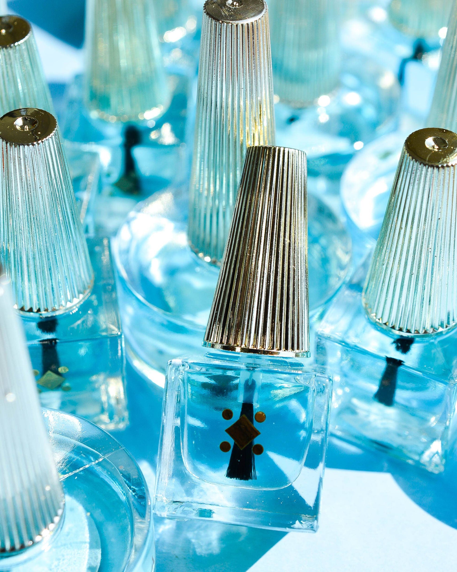 Clear nail polish bottles with gold caps on a blue background