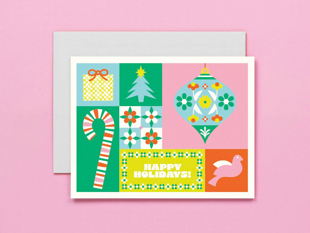 A square holiday greeting card with a retro 1960s-inspired patchwork design, featuring a candy cane, Christmas tree, ornament, gift box, and a bird, with 'HAPPY HOLIDAYS!' printed on it. The card is shown with a light gray envelope against a solid pink background.