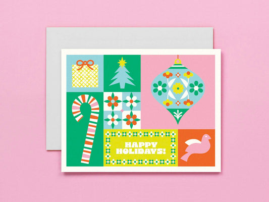 A square holiday greeting card with a retro 1960s-inspired patchwork design, featuring a candy cane, Christmas tree, ornament, gift box, and a bird, with 'HAPPY HOLIDAYS!' printed on it. The card is shown with a light gray envelope against a solid pink background.