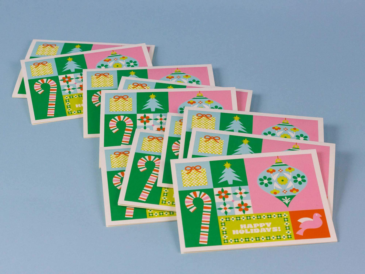 A set of Christmas greeting cards with a retro patchwork design featuring green, pink, yellow, and white holiday motifs like candy canes, ornaments, gifts, and trees, arranged on a light blue background.