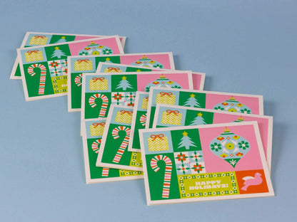 A set of Christmas greeting cards with a retro patchwork design featuring green, pink, yellow, and white holiday motifs like candy canes, ornaments, gifts, and trees, arranged on a light blue background.