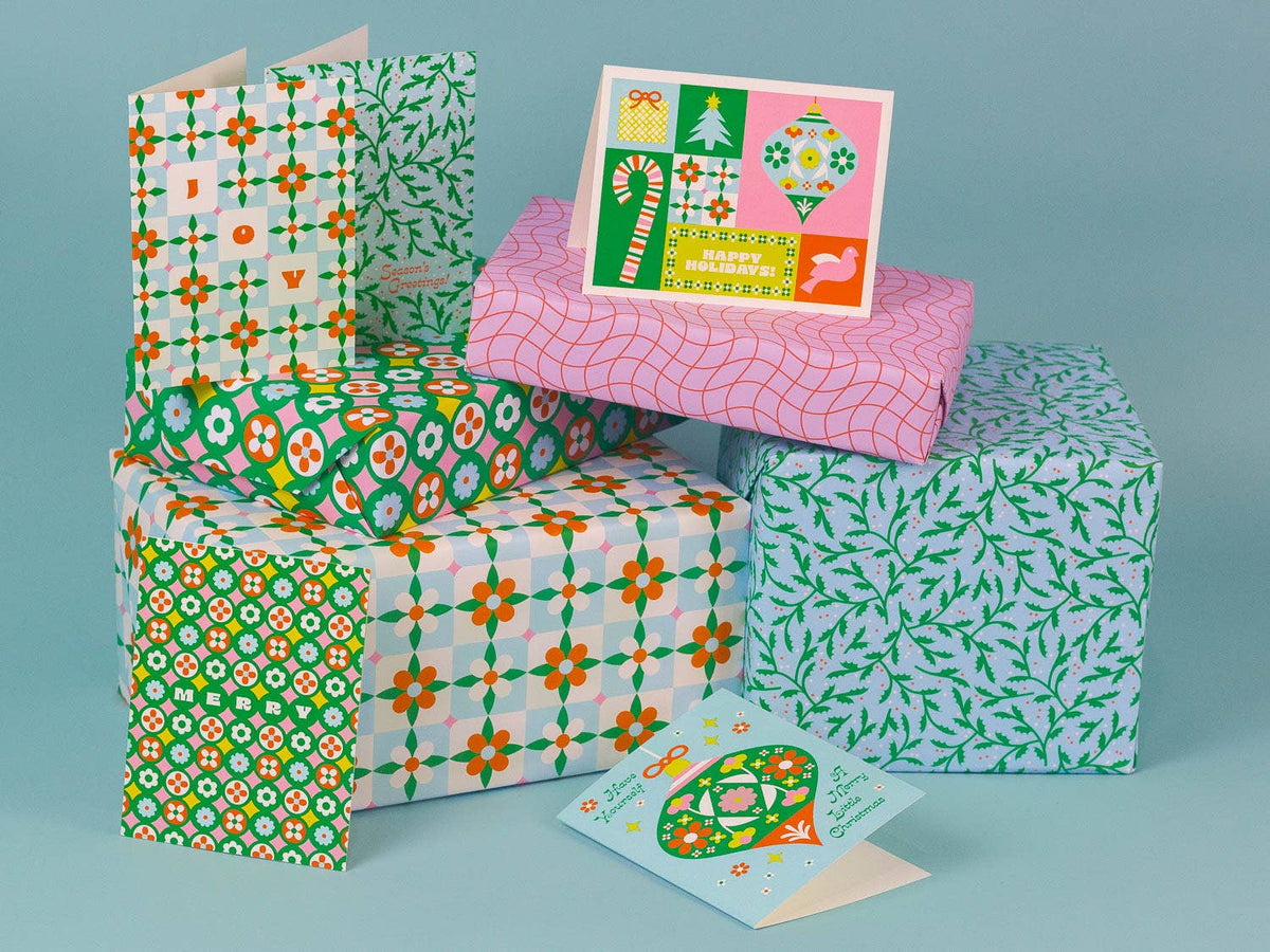 A collection of Christmas-themed gift boxes wrapped in colorful patterned paper, with two matching greeting cards displayed in front, set against a solid light blue background.