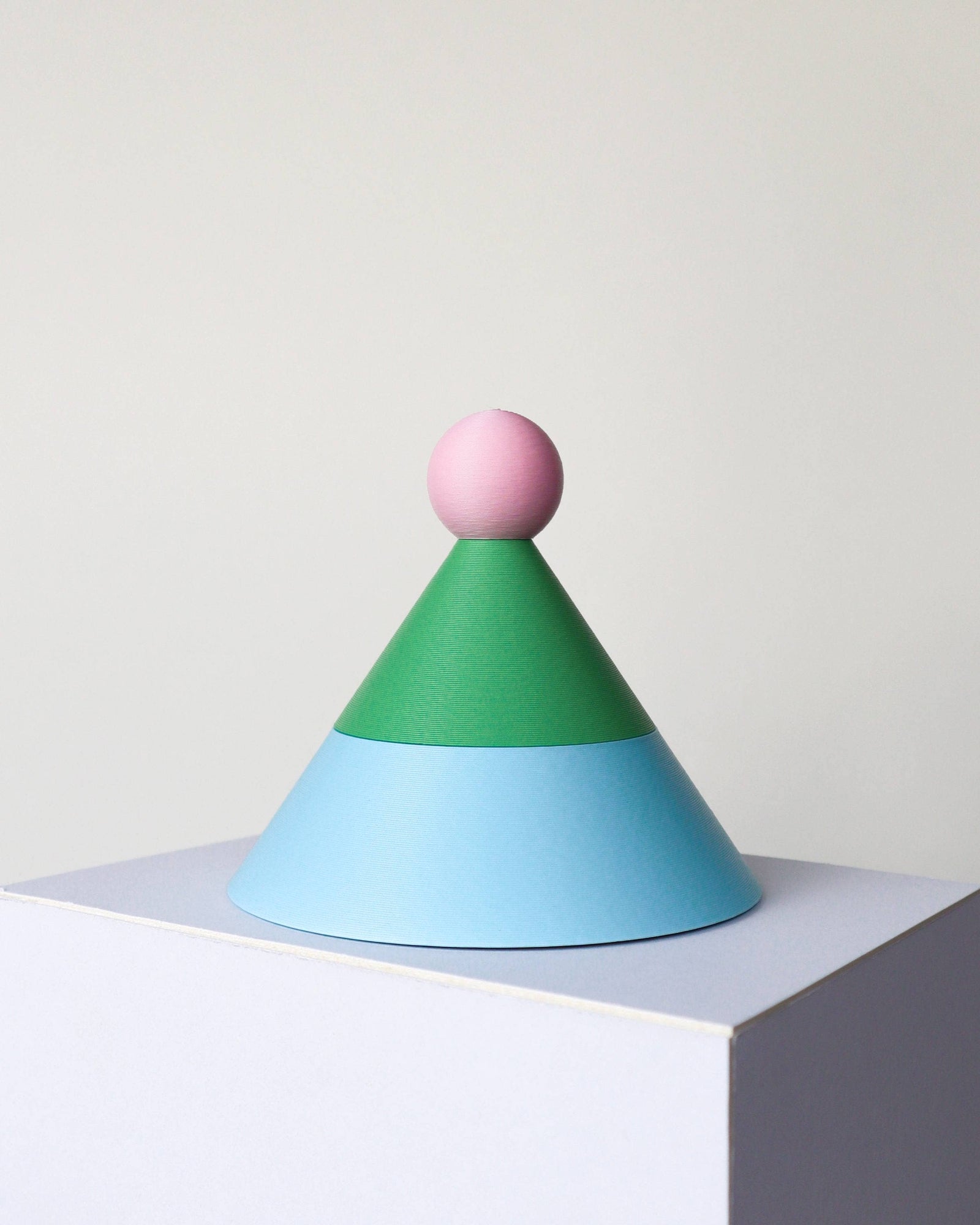 Colorful geometric sculpture with a pink top, green middle, and blue base on a white surface.