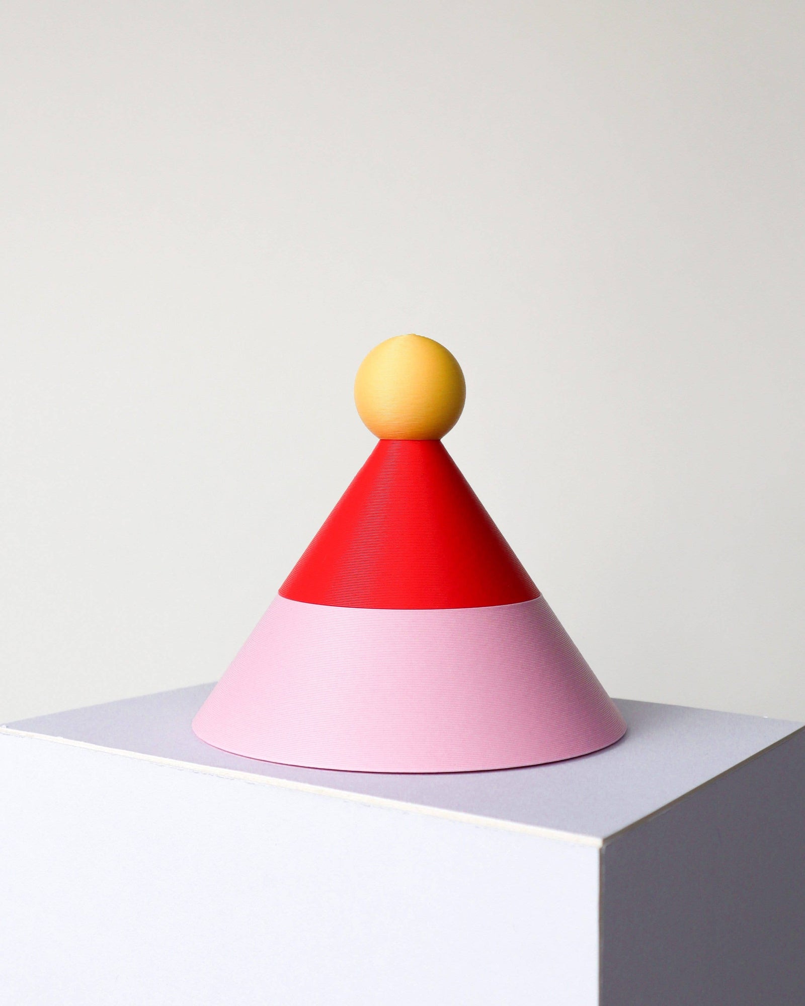Colorful geometric object with a yellow sphere on top, red cone, and pink base on a white background