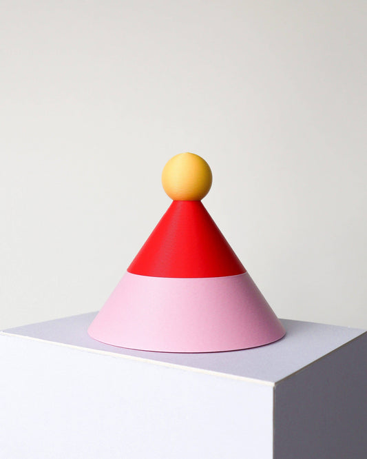 Colorful geometric object with a yellow sphere on top, red cone, and pink base on a white background