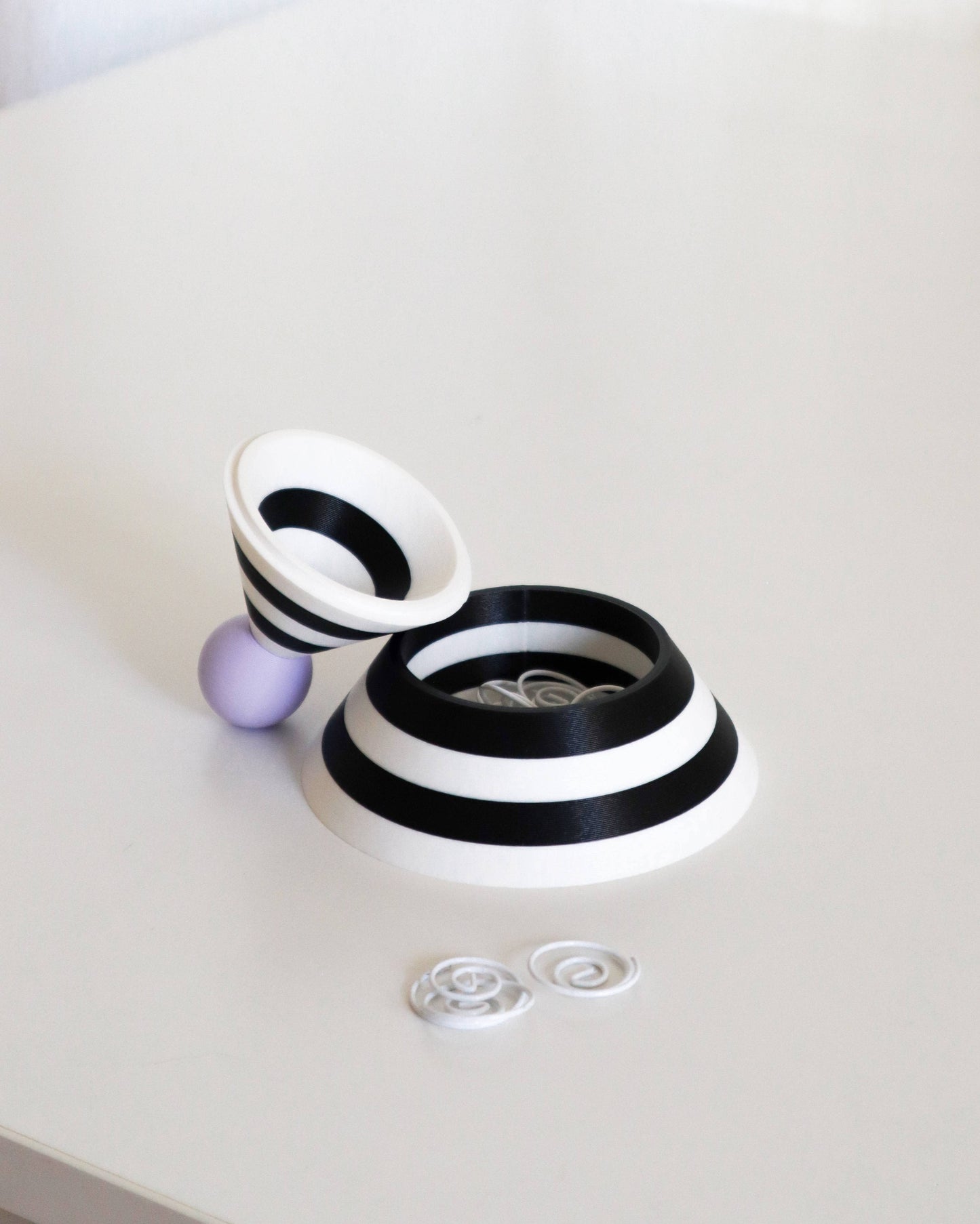 Black and white cylindrical object with a purple sphere on a light gray background