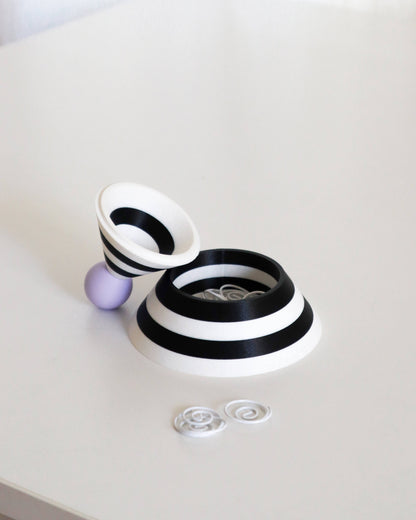 Black and white cylindrical object with a purple sphere on a light gray background