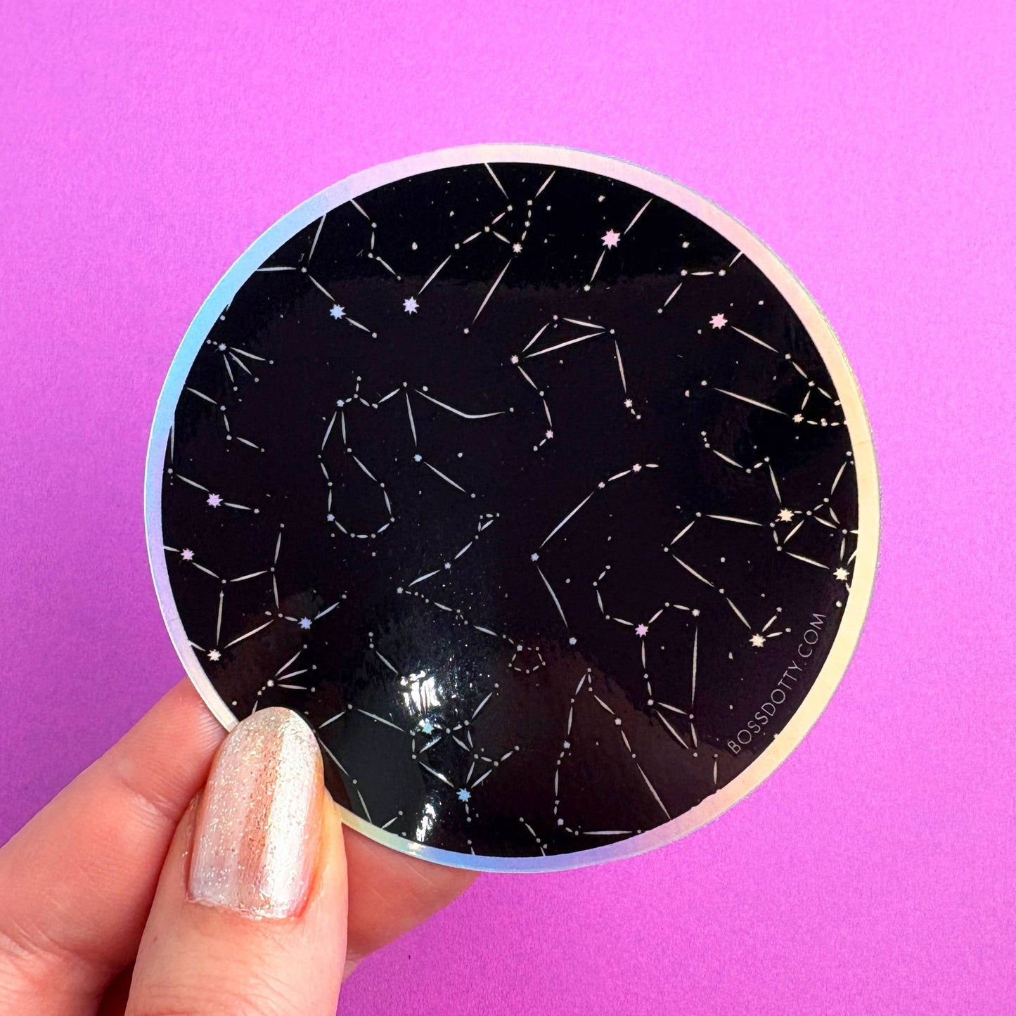Circular sticker with constellation design held against a purple background