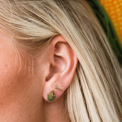 Close-up of an ear wearing a gold earring with green accents and 'tacos' , Corn on the Cob Enamel Stud Earrings Larissa Lodenengraved.