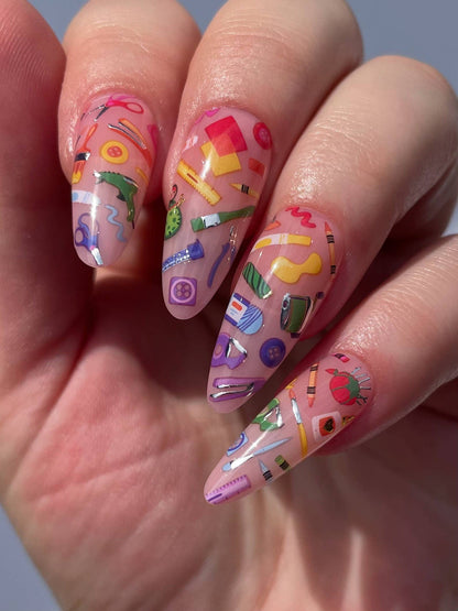 Nails with colorful school-themed design held in a hand against a neutral background