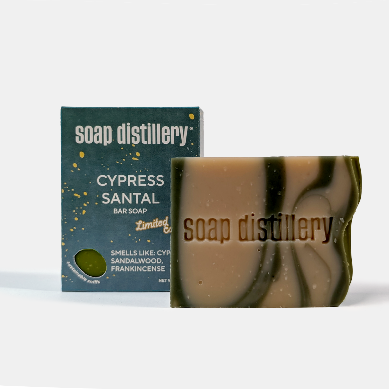 A bar of soap and its packaging box from the brand 'soap distillery'. The box is dark teal with white text and gold speckles, labeled 'CYPRESS SANTAL BAR SOAP'.
