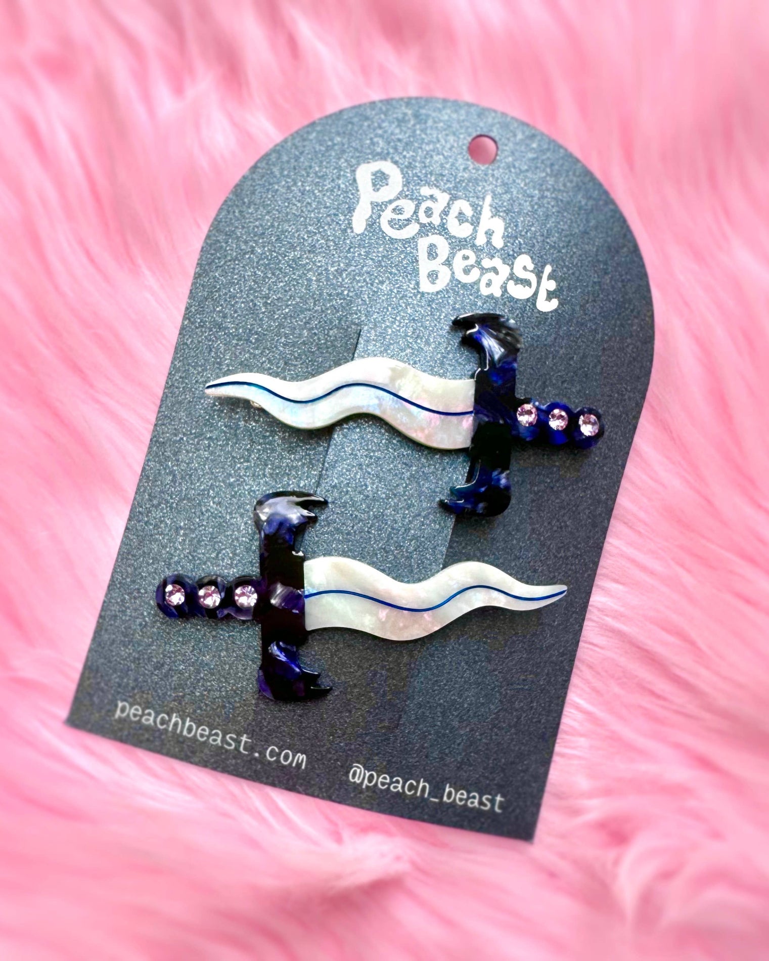 Pair of dagger hair clips on a 'Peach Beast' branded card against a pink background
