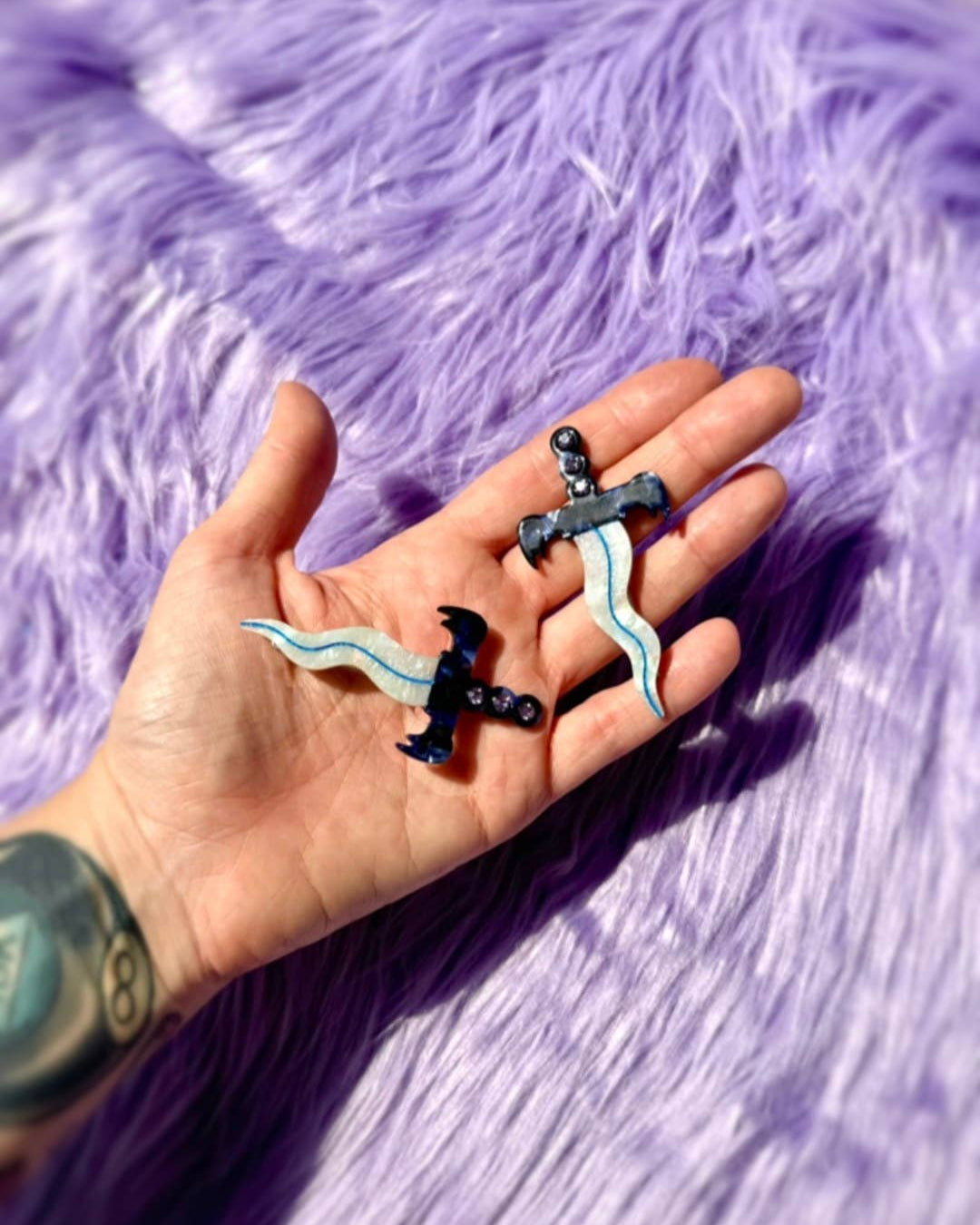 Hand holding two dagger hair clips on a purple textured background