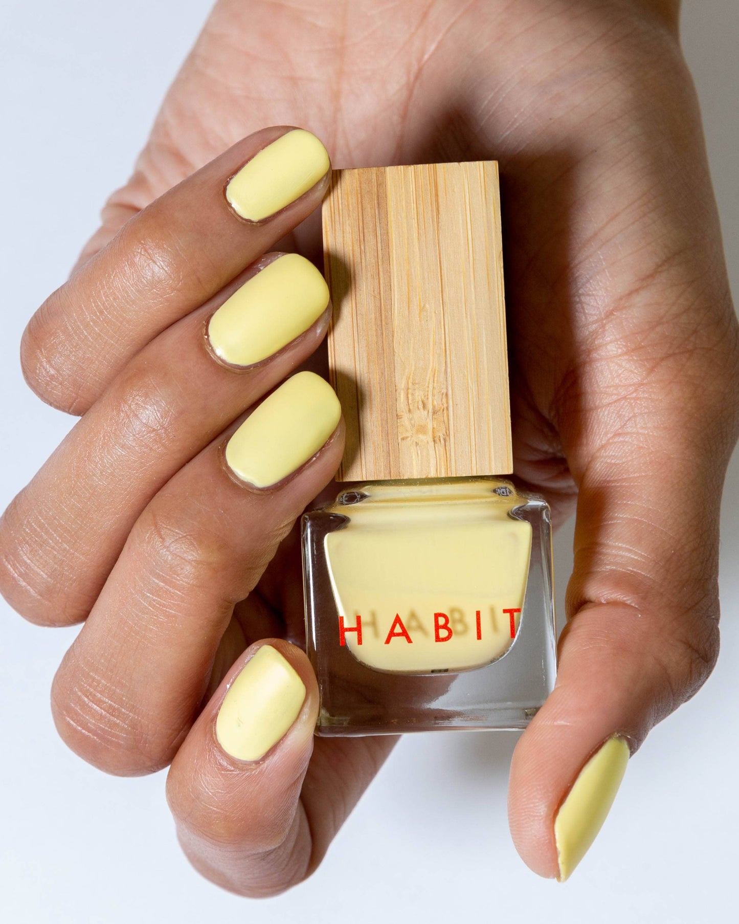 Hand with yellow nail polish holding a bottle of 'Habit' nail polish.