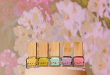 Five small bottles of nail polish with wooden caps on a floral background