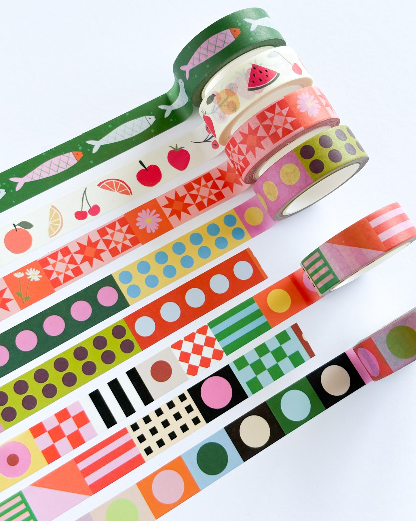 A set of colorful washi tapes with various patterns including fruit, geometric shapes, stripes, and dots, arranged diagonally on a white background.