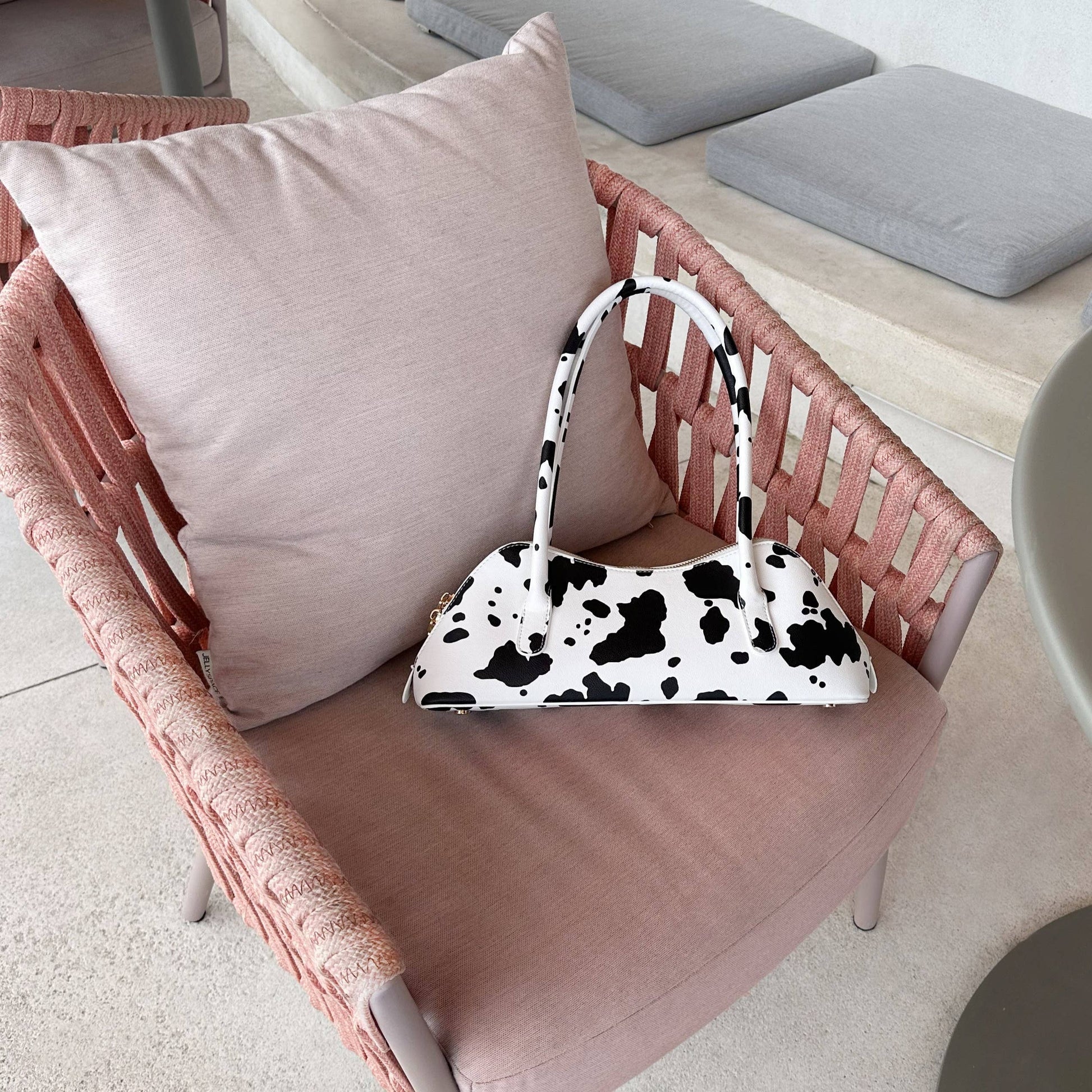Cow print handbag on a pink chair with cushions in a minimalistic room.