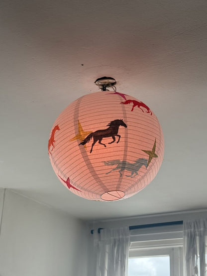 A spherical pink paper lantern ceiling light with printed animal silhouettes, hanging from a ceiling in a room with a window and white curtains.
