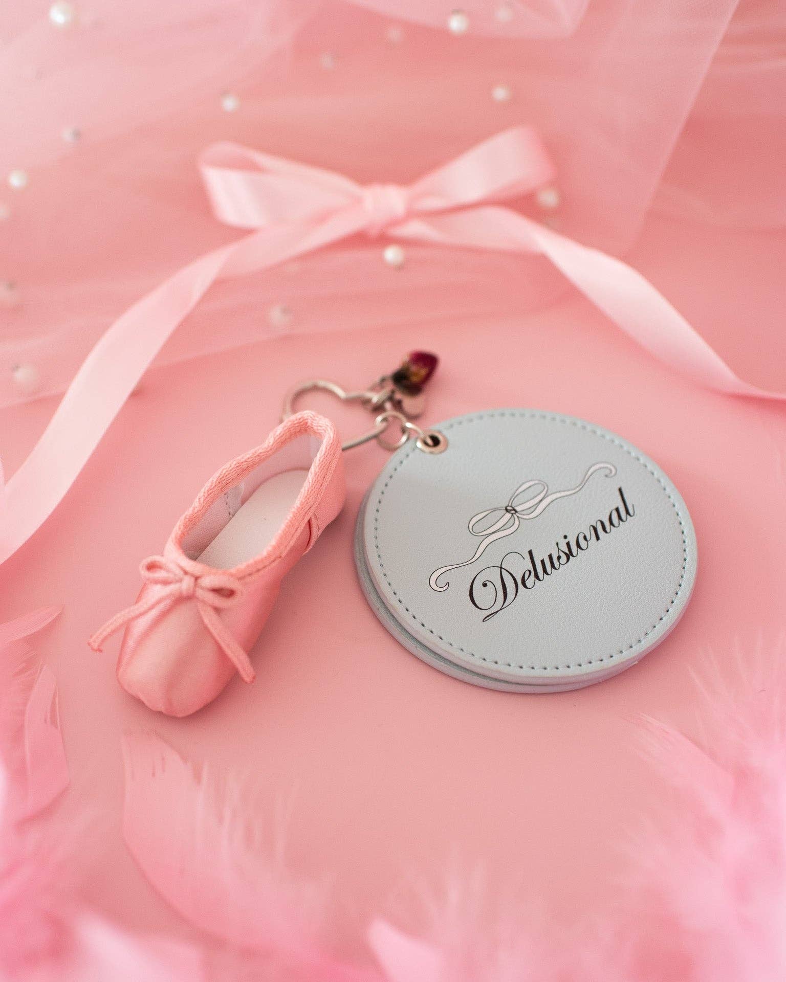 Keychain with pink ballet shoe design and 'Delusional' tag on a pink background