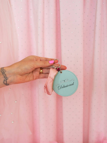 Hand holding a pink keychain with a teal tag against a pink curtain background Delusional Mirror Keychain