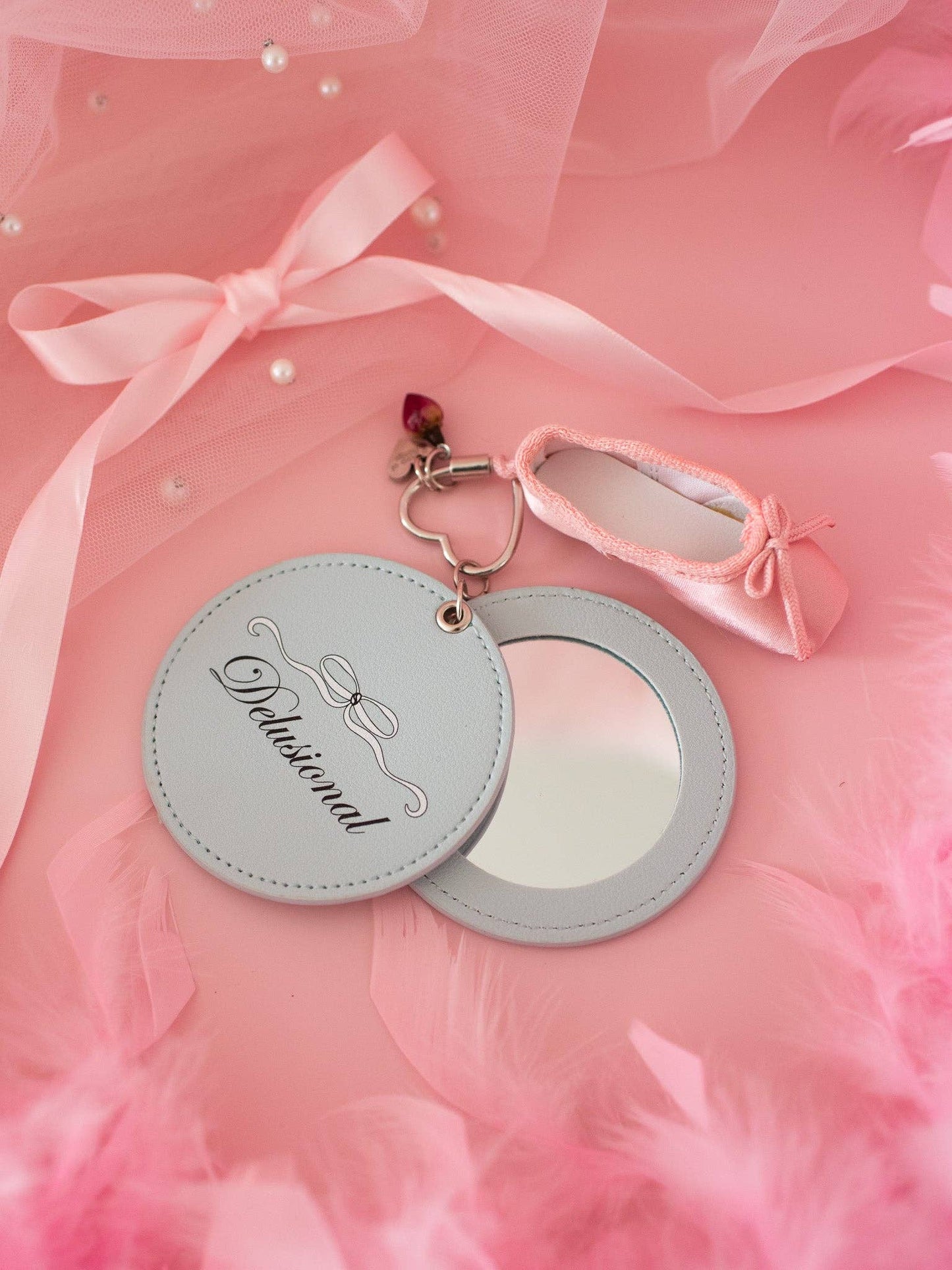 Round mirror with decorative keychain on a pink fabric background Delusional Mirror Keychain