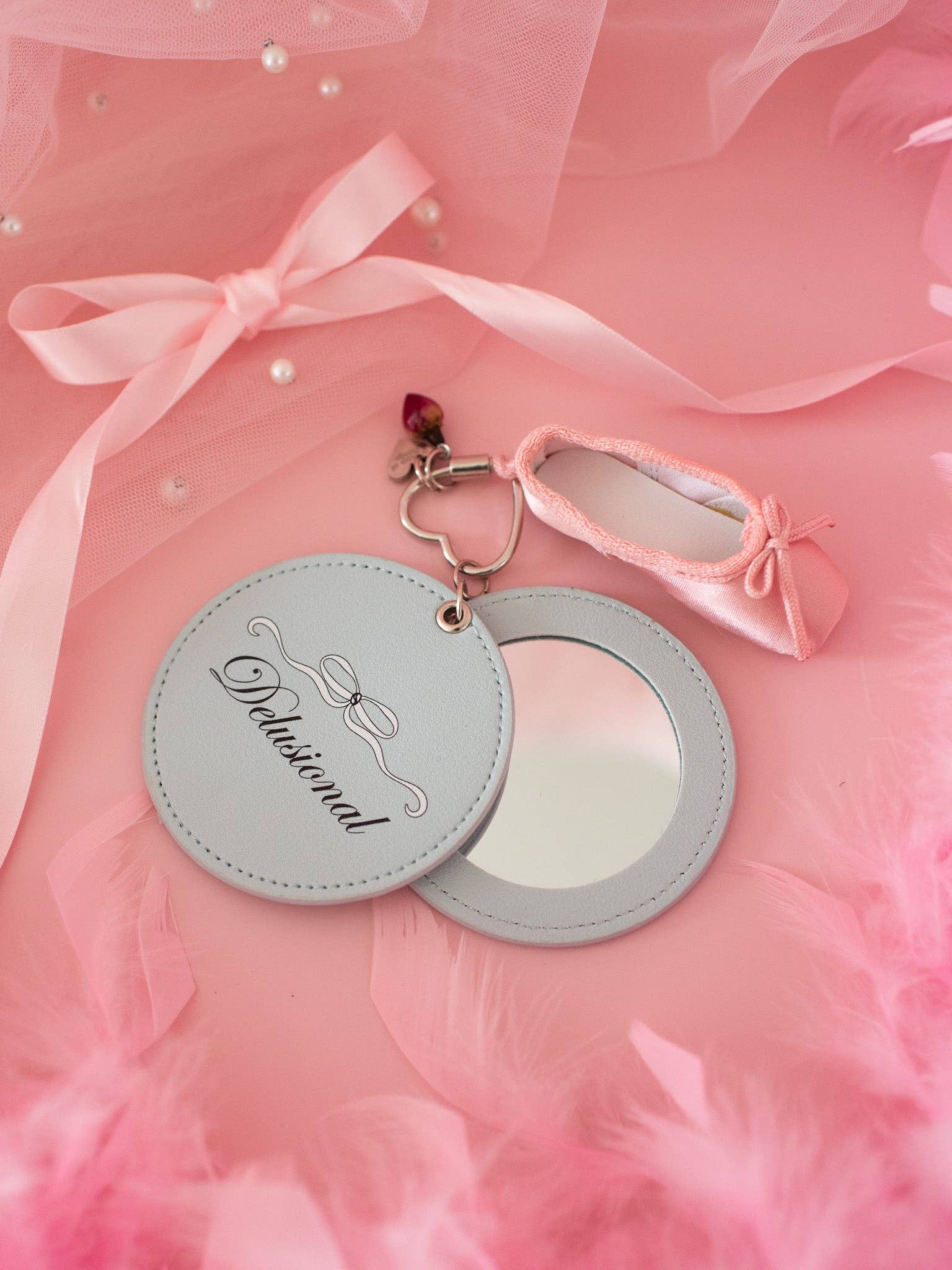 Round mirror with decorative keychain on a pink fabric background Delusional Mirror Keychain