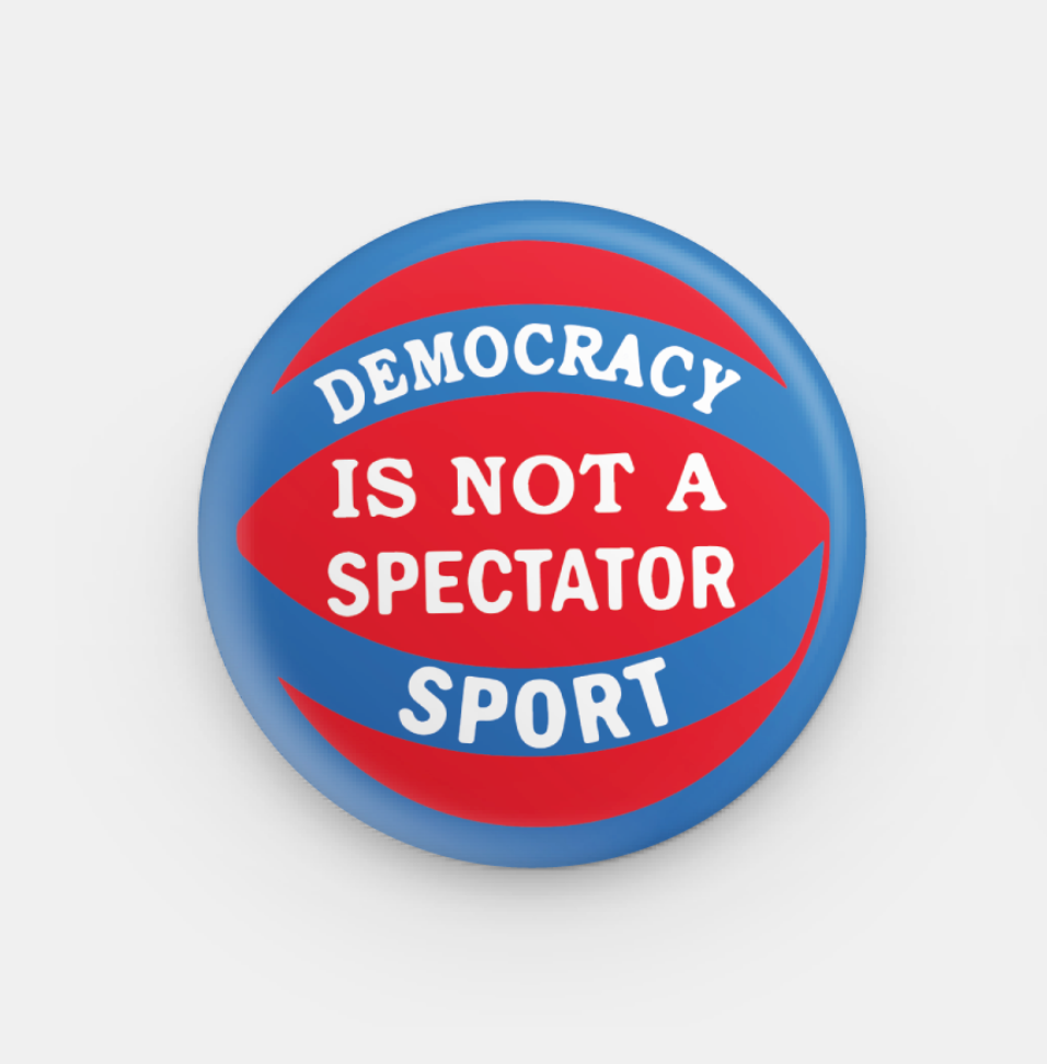 Button badge with 'Democracy is not a spectator sport' text on a white background