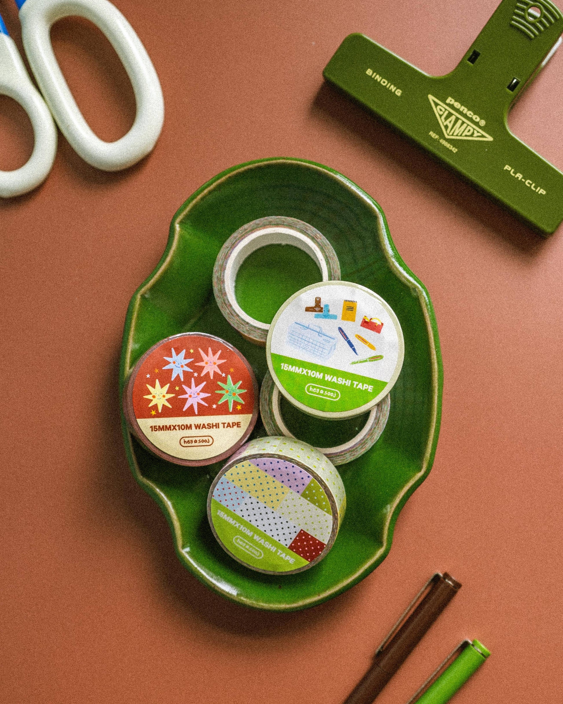 Assorted tape rolls on a green tray with scissors and a paper trimmer on a brown background
