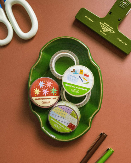 Assorted tape rolls on a green tray with scissors and a paper trimmer on a brown background