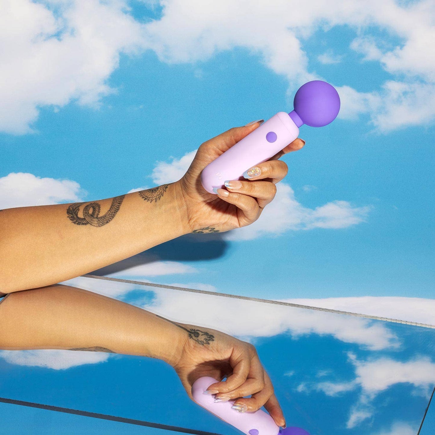 Hand holding a purple and white device against a blue sky with clouds