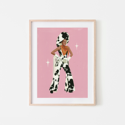 A framed art print featuring a stylized illustration ofDIANA ROSS in a black-and-white cow-print outfit against a pink background, displayed in a light wood frame on a white wall.