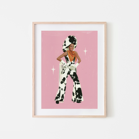 A framed art print featuring a stylized illustration ofDIANA ROSS in a black-and-white cow-print outfit against a pink background, displayed in a light wood frame on a white wall.