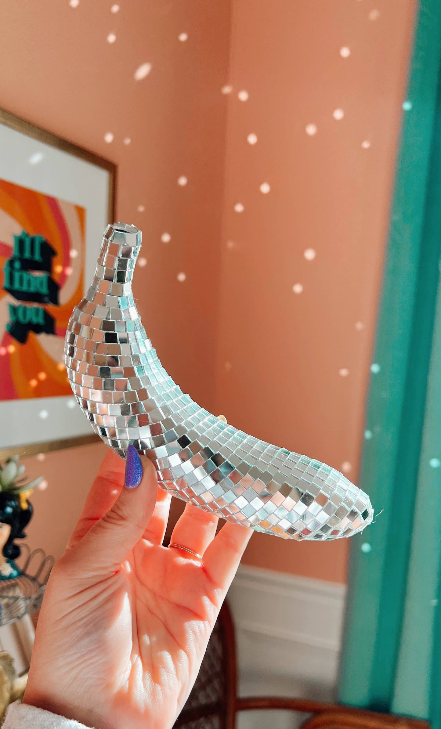 Silver disco banana held in front of a colorful wall with abstract art.