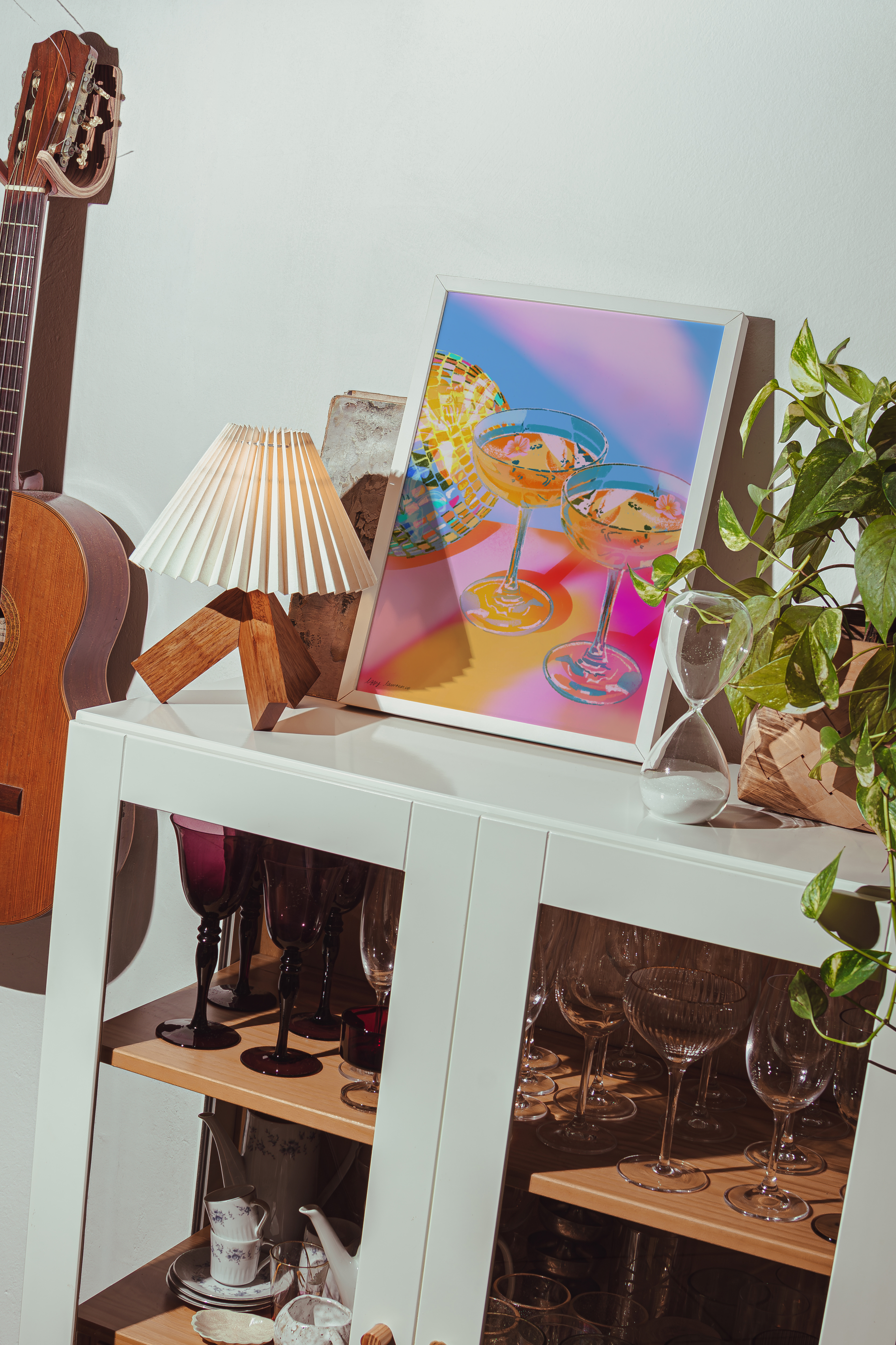 White cabinet with a guitar, lamp, and colorful painting on a white wall.