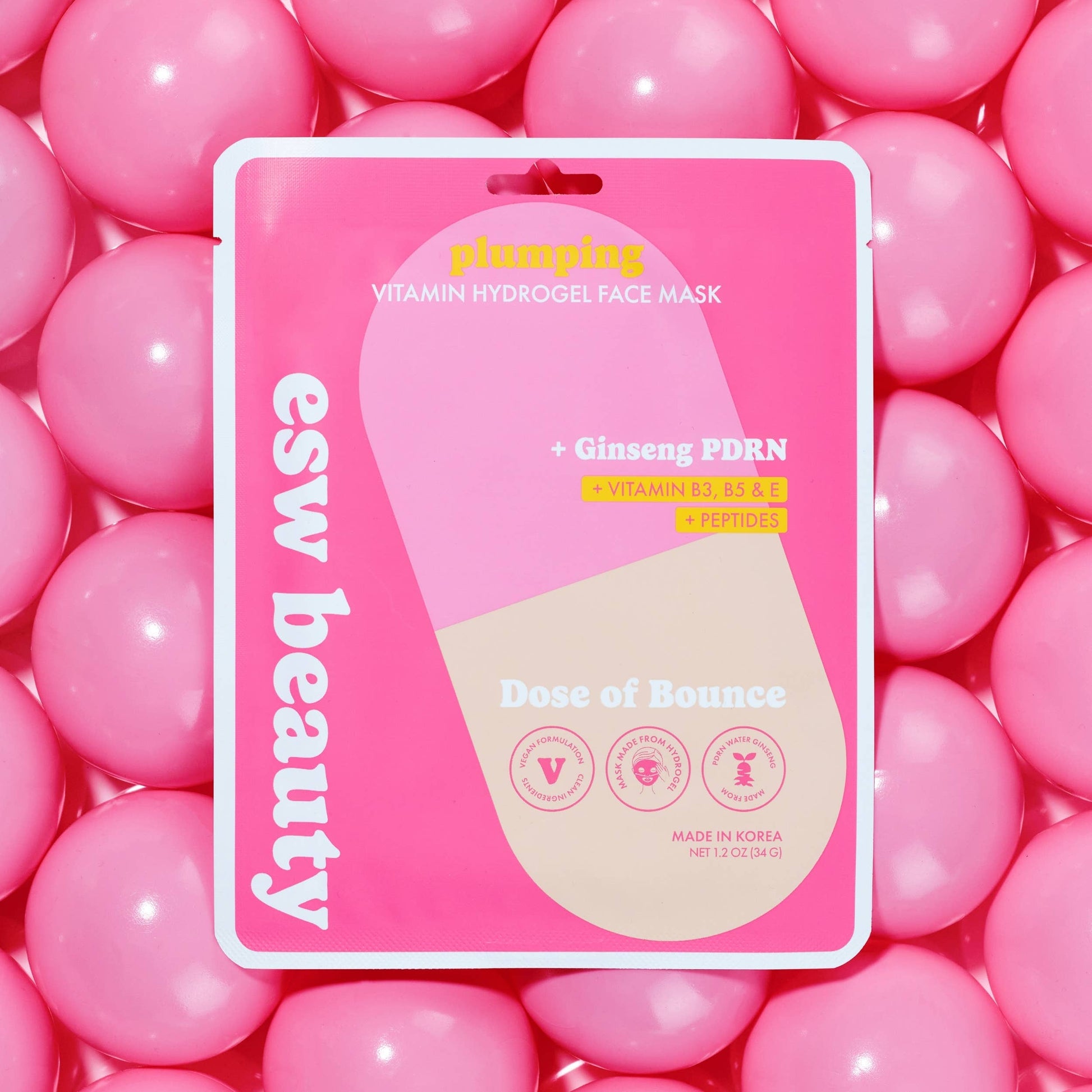A pink and beige blister pack of esw beauty 'Dose of Bounce' vitamin hydrogel face mask, surrounded by a bed of pink gel balls. The packaging features a large pill-shaped graphic and text highlighting key ingredients like Ginseng PDRN.