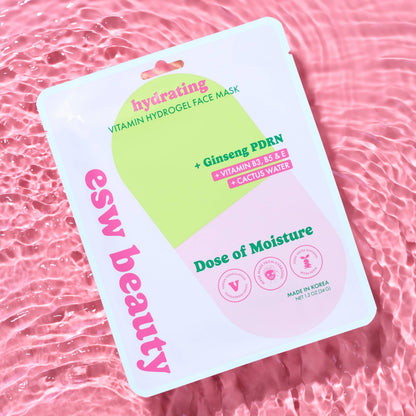 A sheet mask package labeled 'ess beauty hydrating Vitamin Hydrogel Face Mask' with pink and green graphics, photographed on a pink water-texture background.