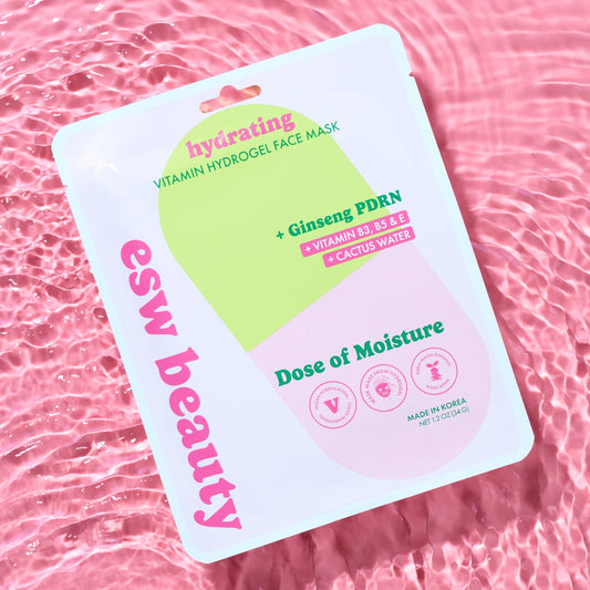 A sheet mask package labeled 'ess beauty hydrating Vitamin Hydrogel Face Mask' with pink and green graphics, photographed on a pink water-texture background.