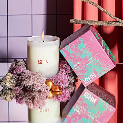 Candle with 'LOHN' branding on a decorative surface with a pink and green box.