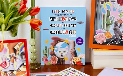 Collage book and craft materials on a table with flowers and framed pictures.