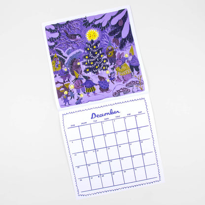 A double-sided desk calendar page set shown on a light gray background. The top page features a whimsical purple-toned winter forest illustration with a glowing Christmas tree and figures, while the bottom page shows a blue-lined December calendar grid.