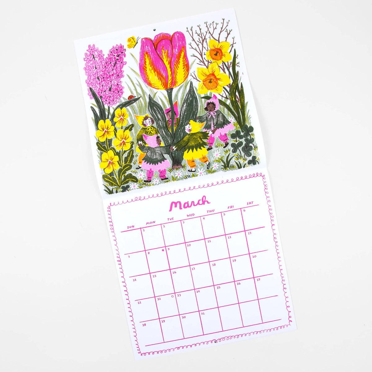 A hanging calendar page with a colorful floral illustration on the top half and a pink calendar grid for March on the bottom half, photographed on a clean white background.