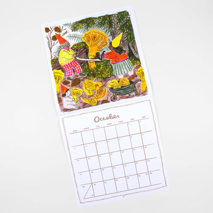 A single illustrated calendar page showing a whimsical forest scene with large yellow mushrooms, a person in a red-and-white checkered shirt, and a calendar grid labeled October below, photographed on a light neutral background.