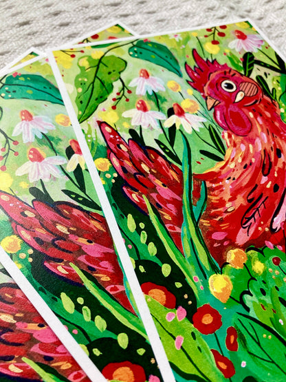 Three illustrated art cards featuring a vibrant red rooster among green leaves and small white flowers, fanned out on a light gray textured surface.