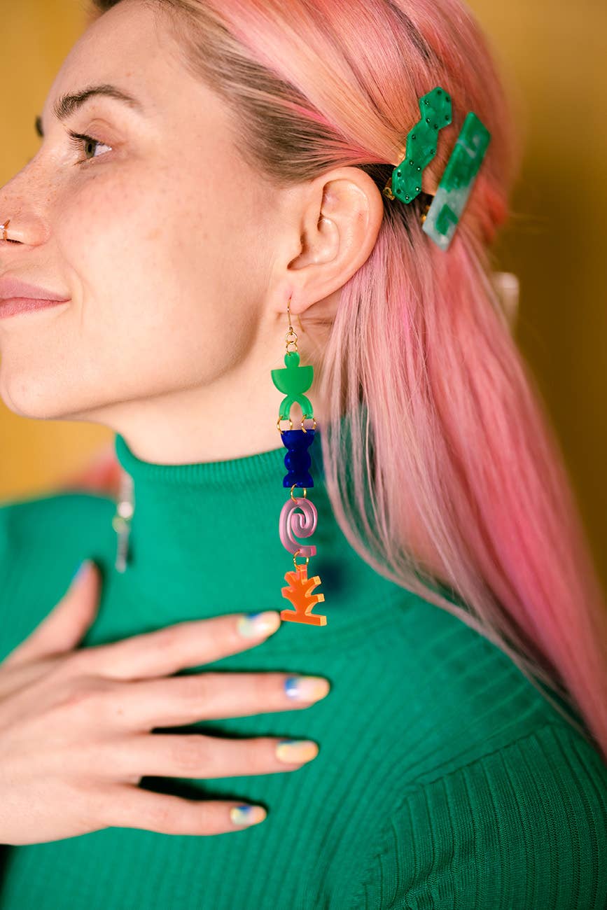 Woman with pink hair wearing colorful earrings against a yellow background