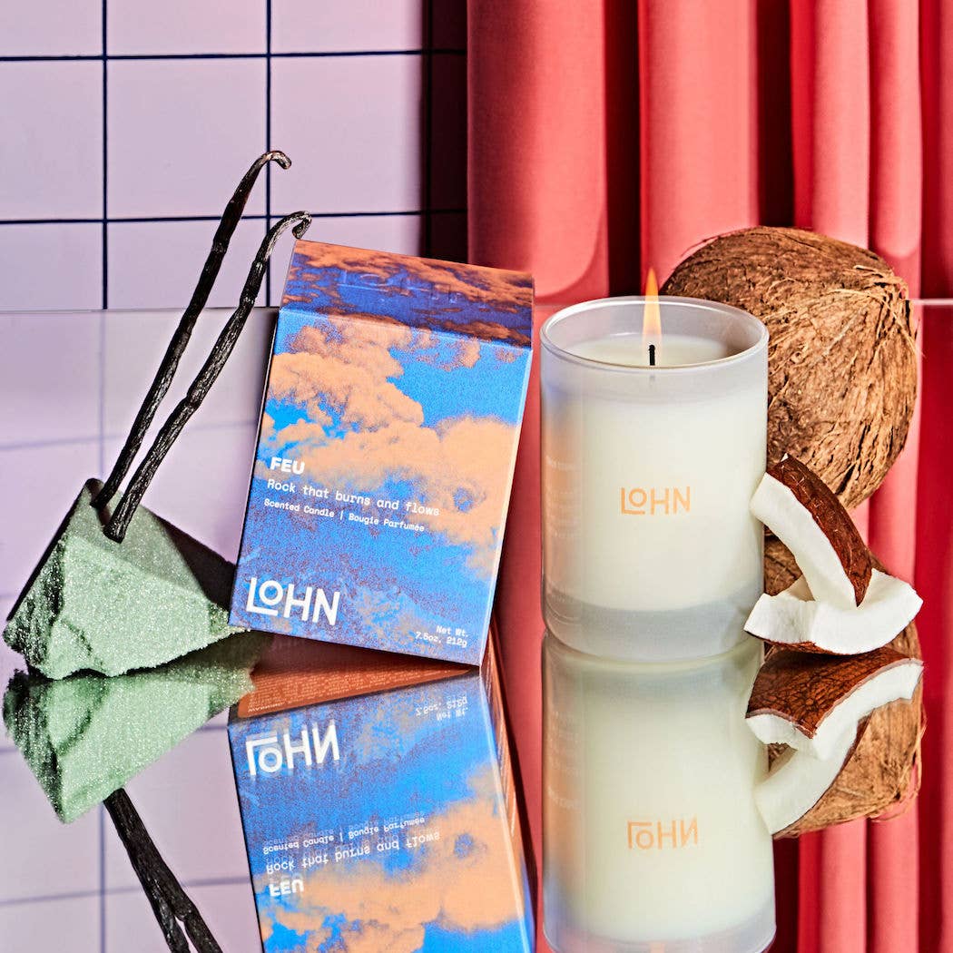 LOHN candle with packaging, vanilla bean, and coconut on a reflective surface with a colorful background.